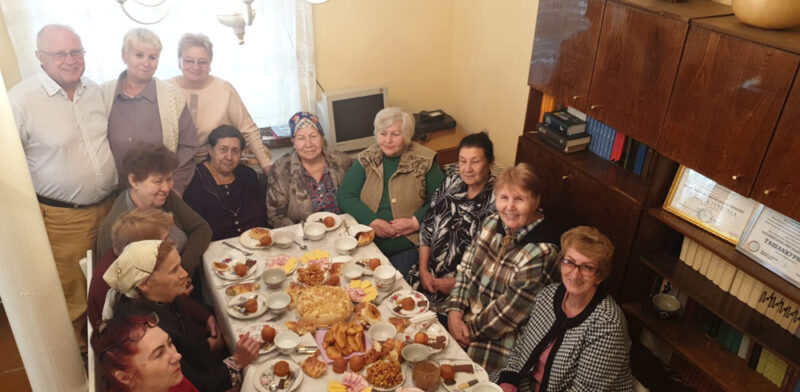 14 Frauen um einen reichlich gedeckten mit Tee und Kuchen