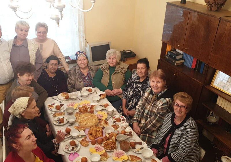 14 Frauen um einen reichlich gedeckten mit Tee und Kuchen